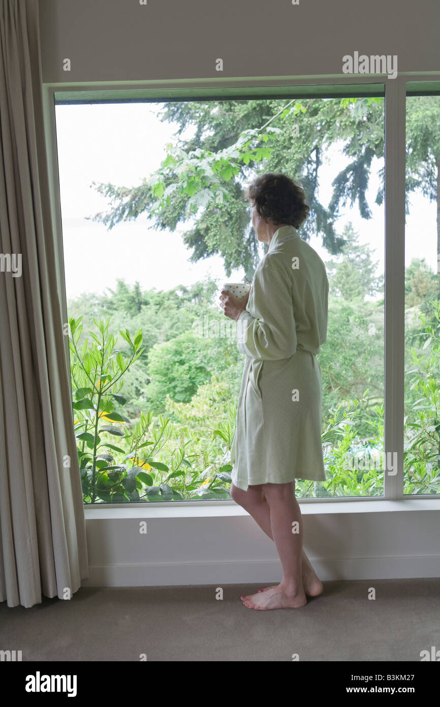 Frau, trinken Kaffee und Blick aus Fenster am Morgen Stockfoto