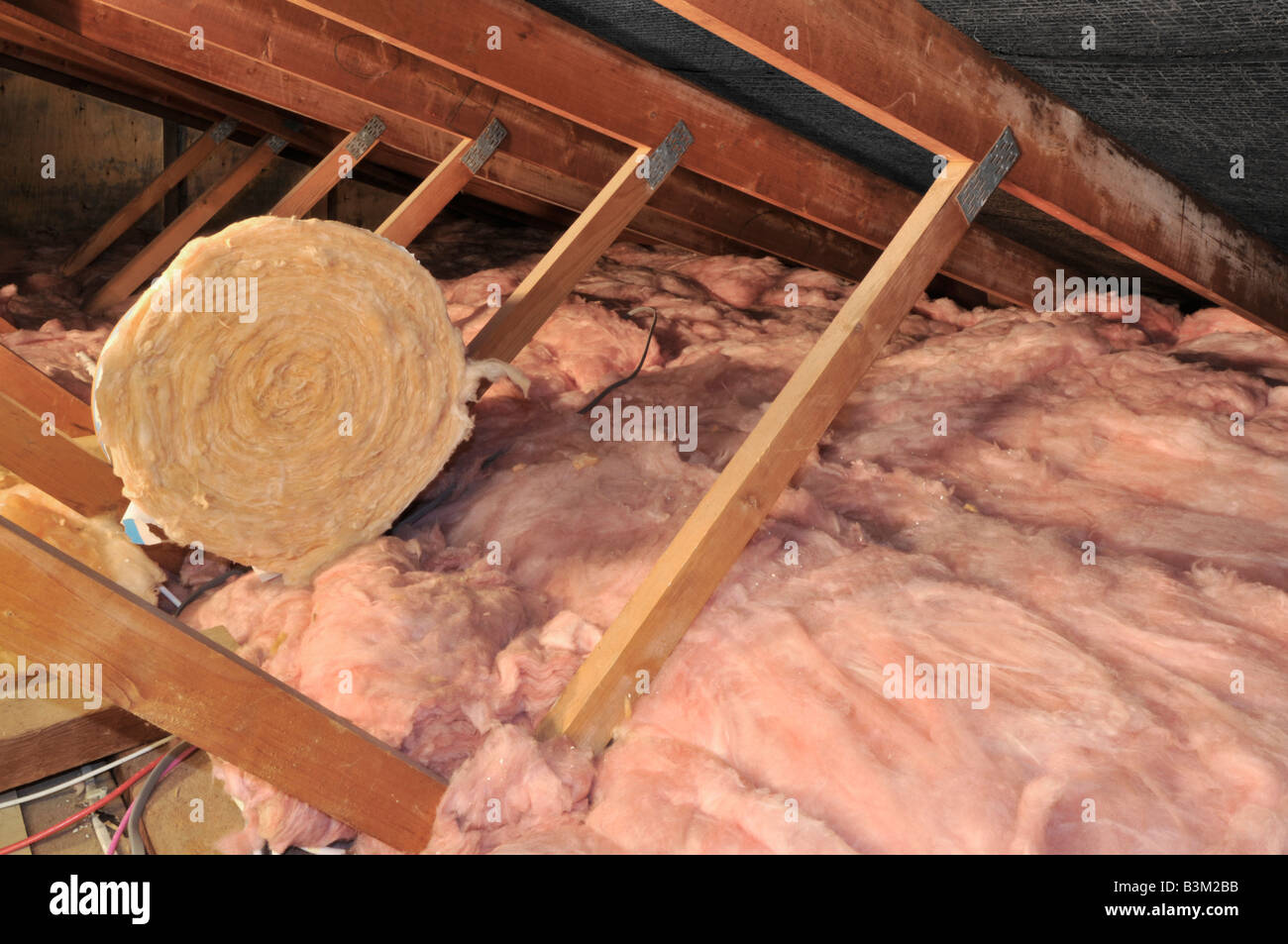 Wohnraum Loft mit niedriger Dachneigung, die Holzdächer zeigen, die Glasfaser verteilen und eine zusammengerollte Dämmdecke über England Großbritannien übrig geblieben ist Stockfoto