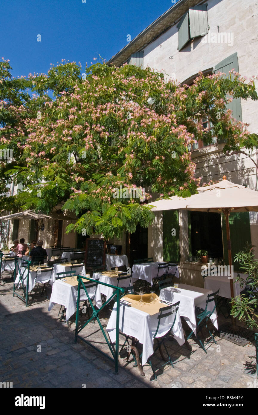 Ein Outdoor-Pflaster-Restaurant in Aigues Mortes in der Camargue Südfrankreich. Von einem blühenden Baum und Sonnenschirmen beschattet. Stockfoto