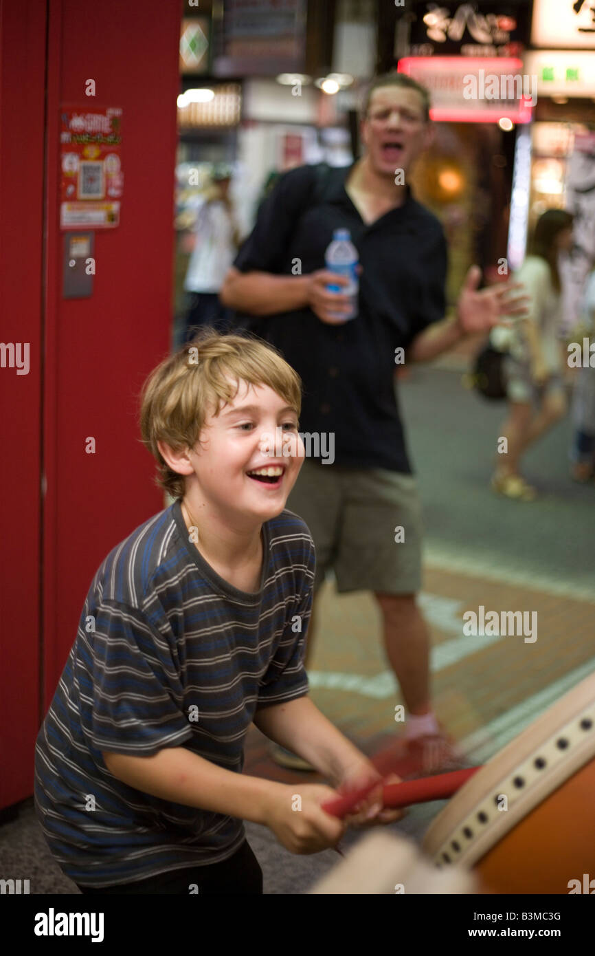 neun Jahre alten amerikanischen jungen spielt Taiko-Trommel-Videospiel in Shinjuku, Tokio, Spielhalle mit Vater ihn anfeuern Stockfoto