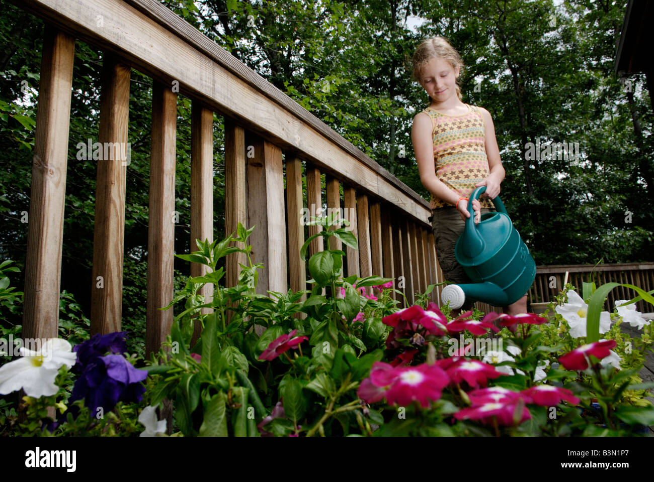 Ein neun Jahres altes Mädchen Wasser Blumen Gemüse und Kräuter in einem städtischen Vorort Garten auf einem hinteren Deck eines Hauses Stockfoto