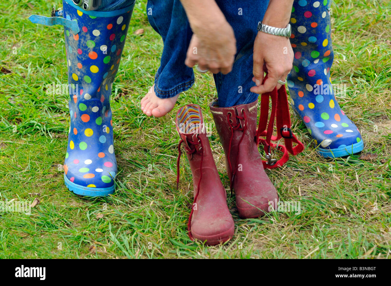 Die Mutter versucht, Schuhe Stiefel Gummistiefel auf Kind Mutter und Kind zu kämpfen Kind Kinder gekleidet zu erhalten Stockfoto