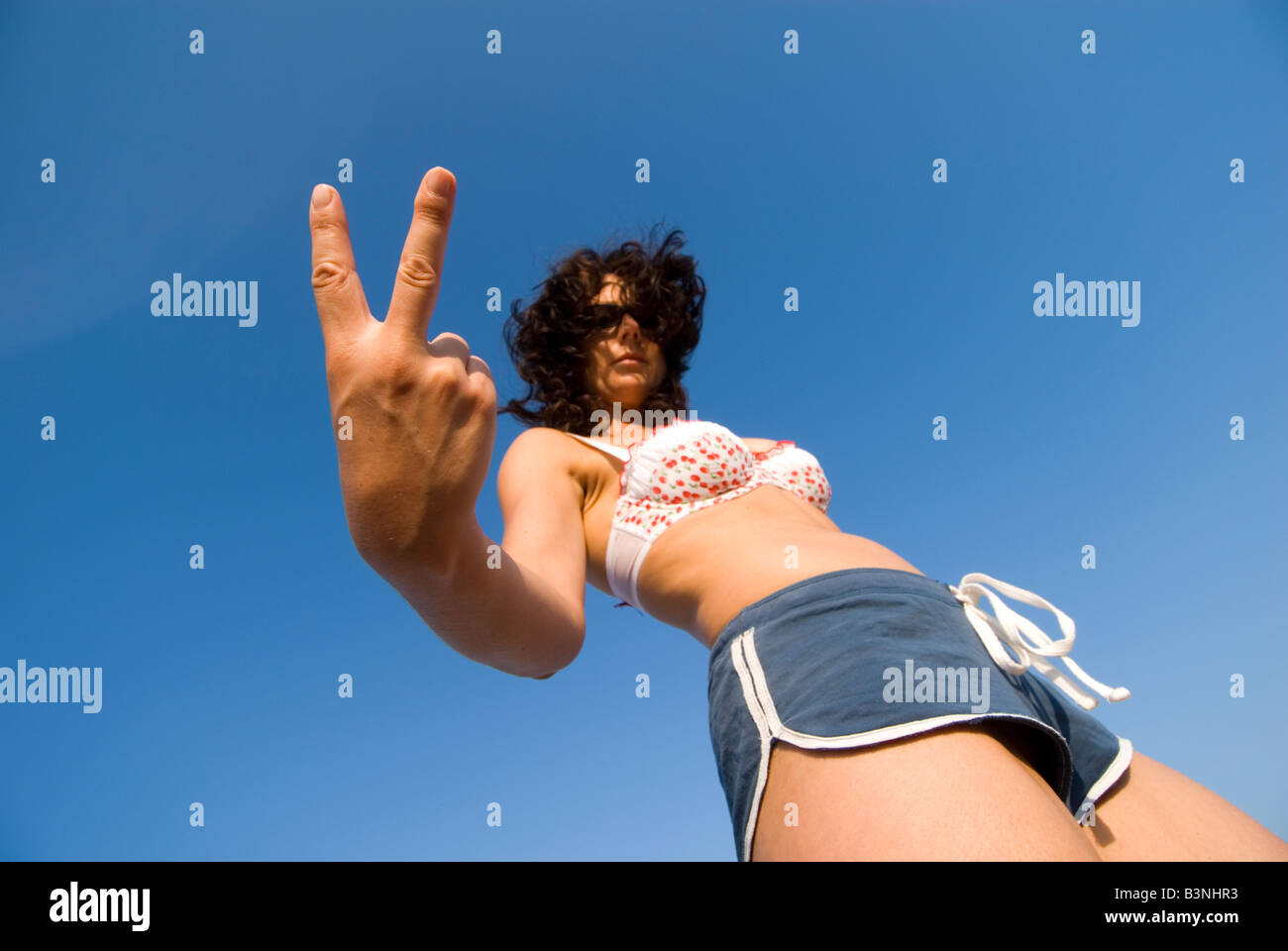 Modell freigegeben weibliche bilden eine missbräuchliche V Zeichen gekleidet im Beachwear niedrigen Winkel Fokus auf Seite Stockfoto
