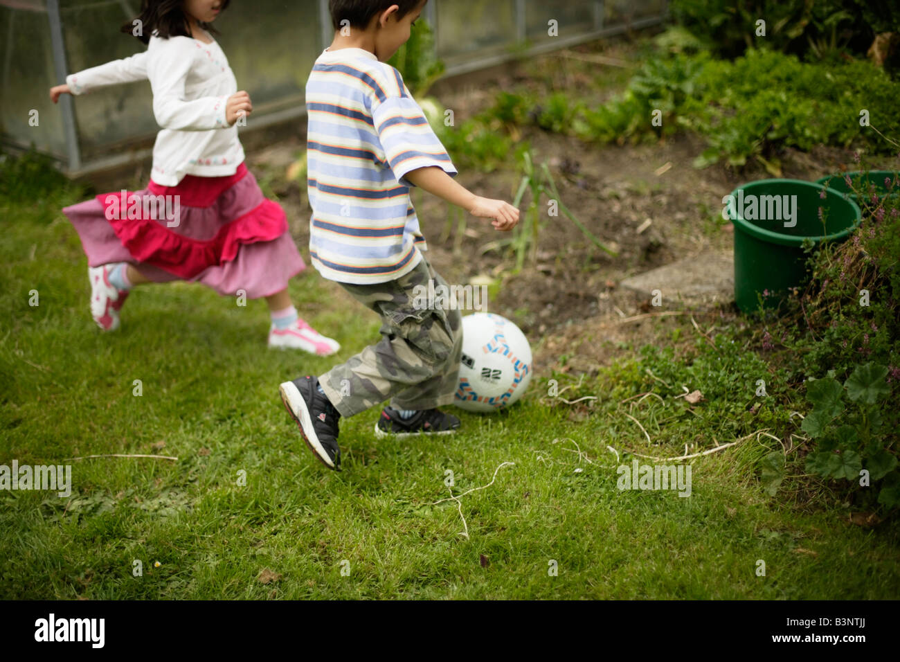 Junge spielen im Alter von sechs und Schwester fünf Fußball treten Ball ins Gemüsebeet Stockfoto