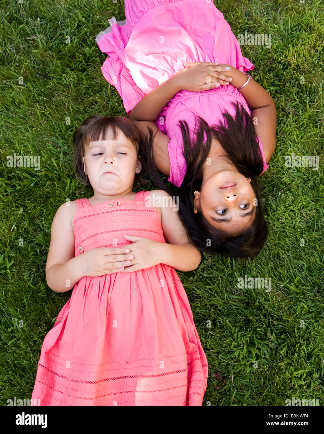 Frienemies?  Ein kleines Mädchen mokiert sich ihre Freundin, wie sie in den Rasen legen. Stockfoto