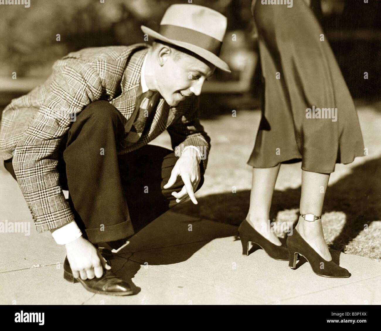 Ein Mann mit einem Tweed-Jacke-Hose und einem Trilby Hut biegt über überprüfen Sie die Zeit auf einer Uhr auf die Knöchel einer Dame der 1930er Jahre getragen Dezember 1937 Stockfoto Ein Mann mit einem Tweed-Jacke-Hose und einem Trilby Hut biegt über überprüfen Sie die Zeit auf einer Uhr auf die Knöchel einer Dame der 1930er Jahre getragen Dezember 1937 Stockfoto