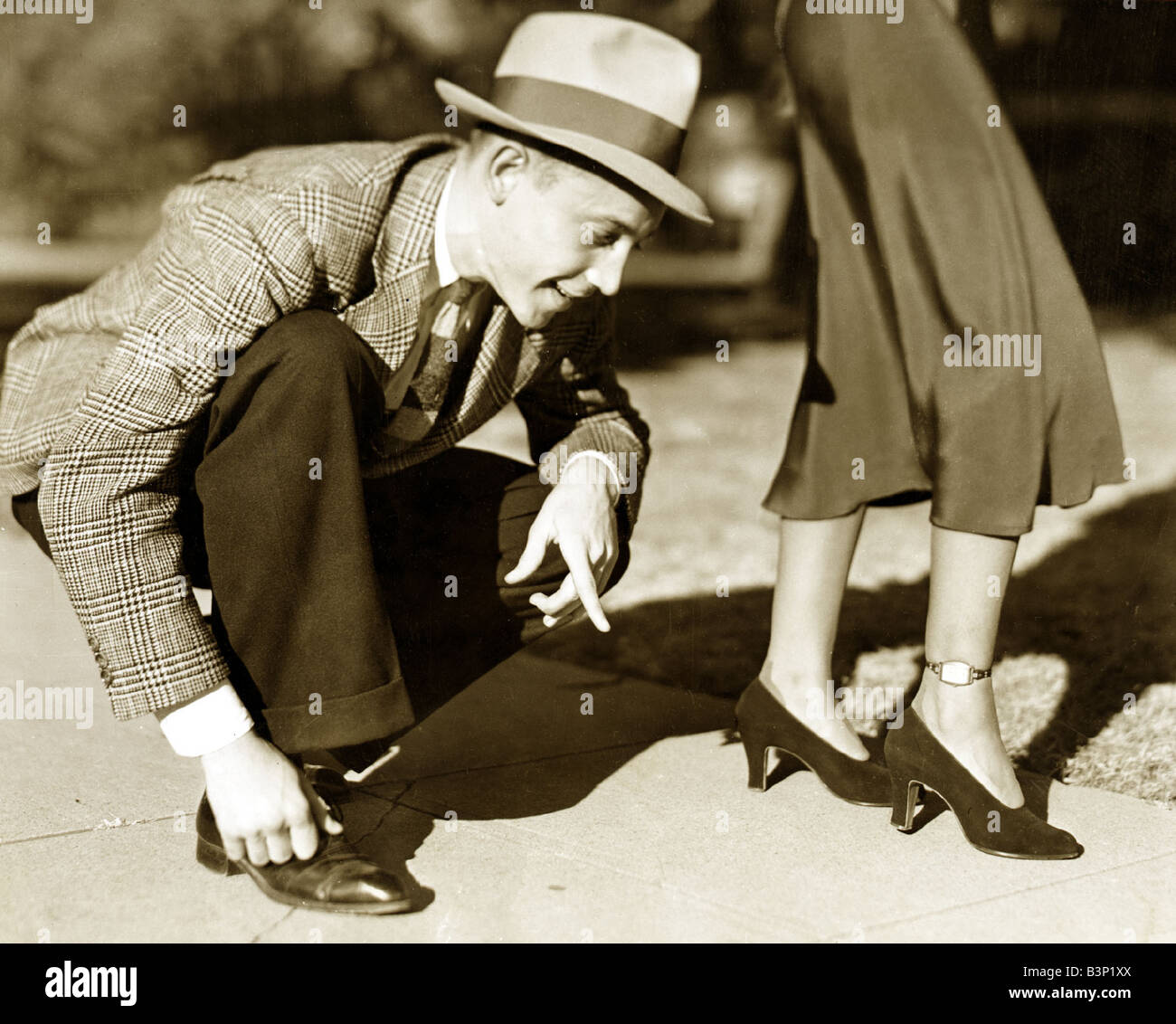 Ein Mann mit einem Tweed-Jacke-Hose und einem Trilby Hut biegt über überprüfen Sie die Zeit auf einer Uhr auf die Knöchel einer Dame der 1930er Jahre getragen Dezember 1937 Stockfoto