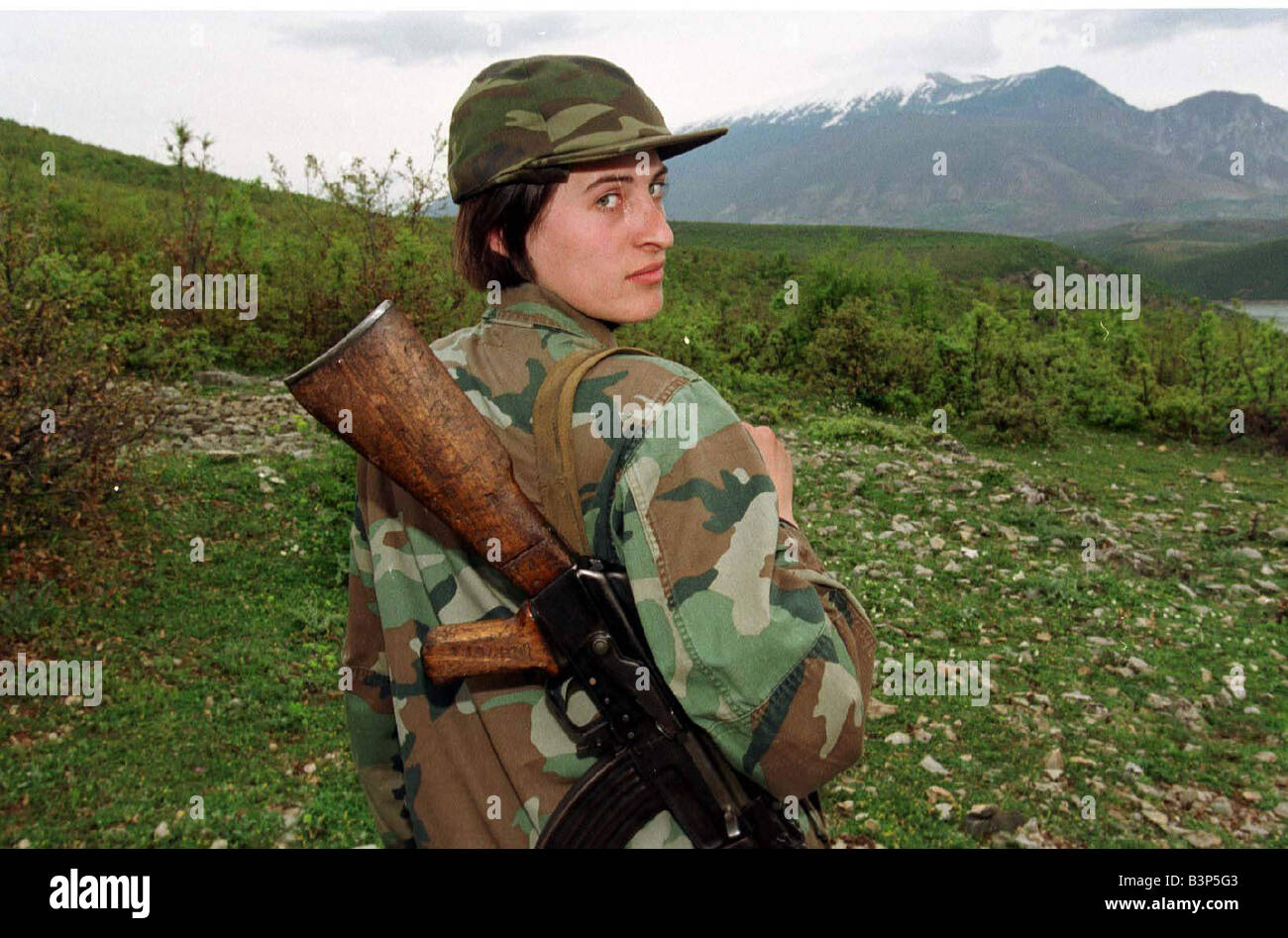 Luljeta Gashi von der Kosovo Befreiungsarmee UCK April 1999 Soldatin mit einem Gewehr über ihre Soldaten zu Fuß über die grüne Landschaft Blick zurück über die Schulter Stockfoto