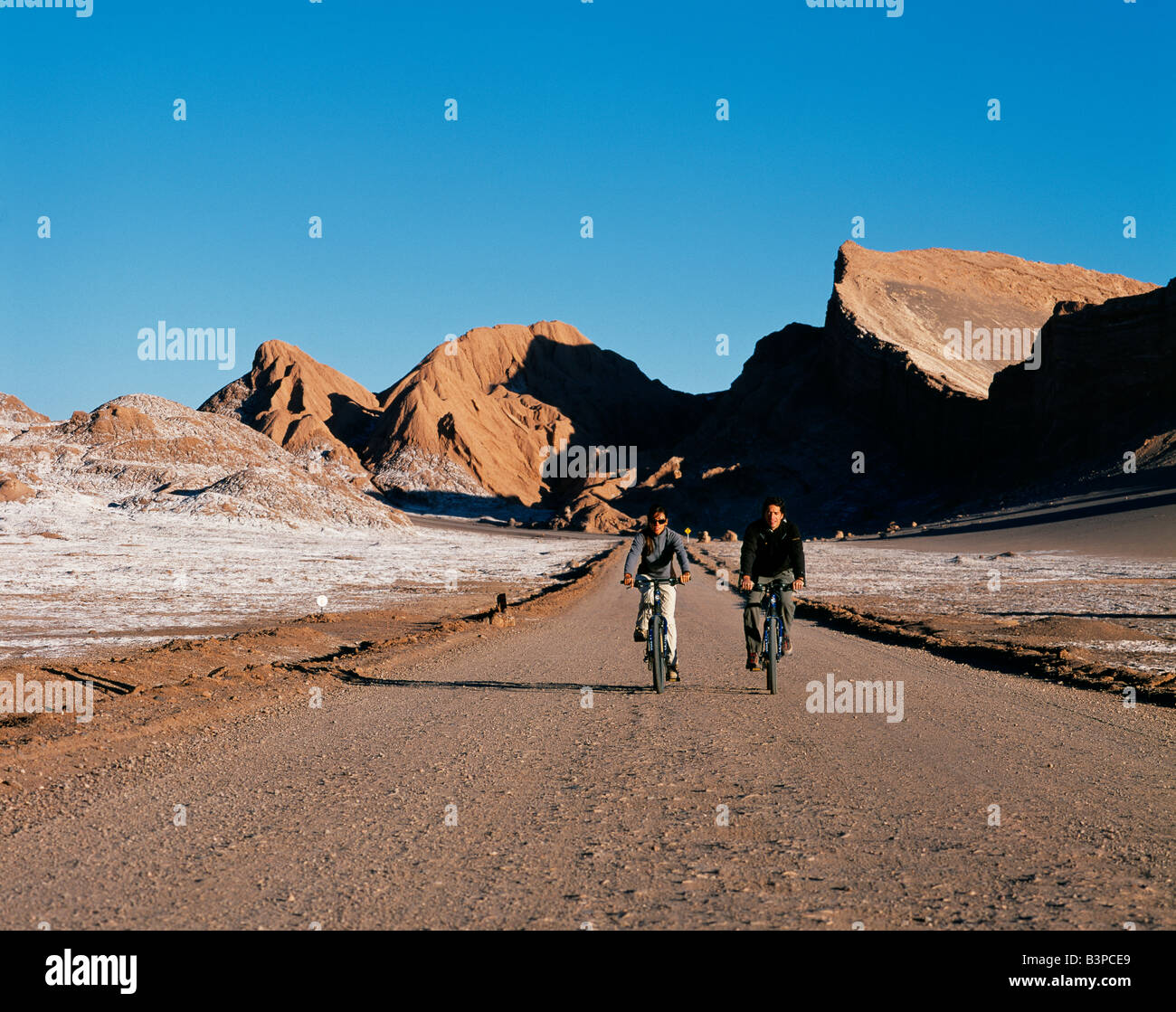Chile, Atacama-Wüste, San Pedro de Atacama. Touristen-Mountainbiken in der eindrucksvollen Landschaft der Moon Valley in der Nähe von San Pedro de Atacama in der Atacama-Wüste, die geprägt ist von Wind erodiert Hügeln und einem mineralischen Käserand Talboden. Stockfoto