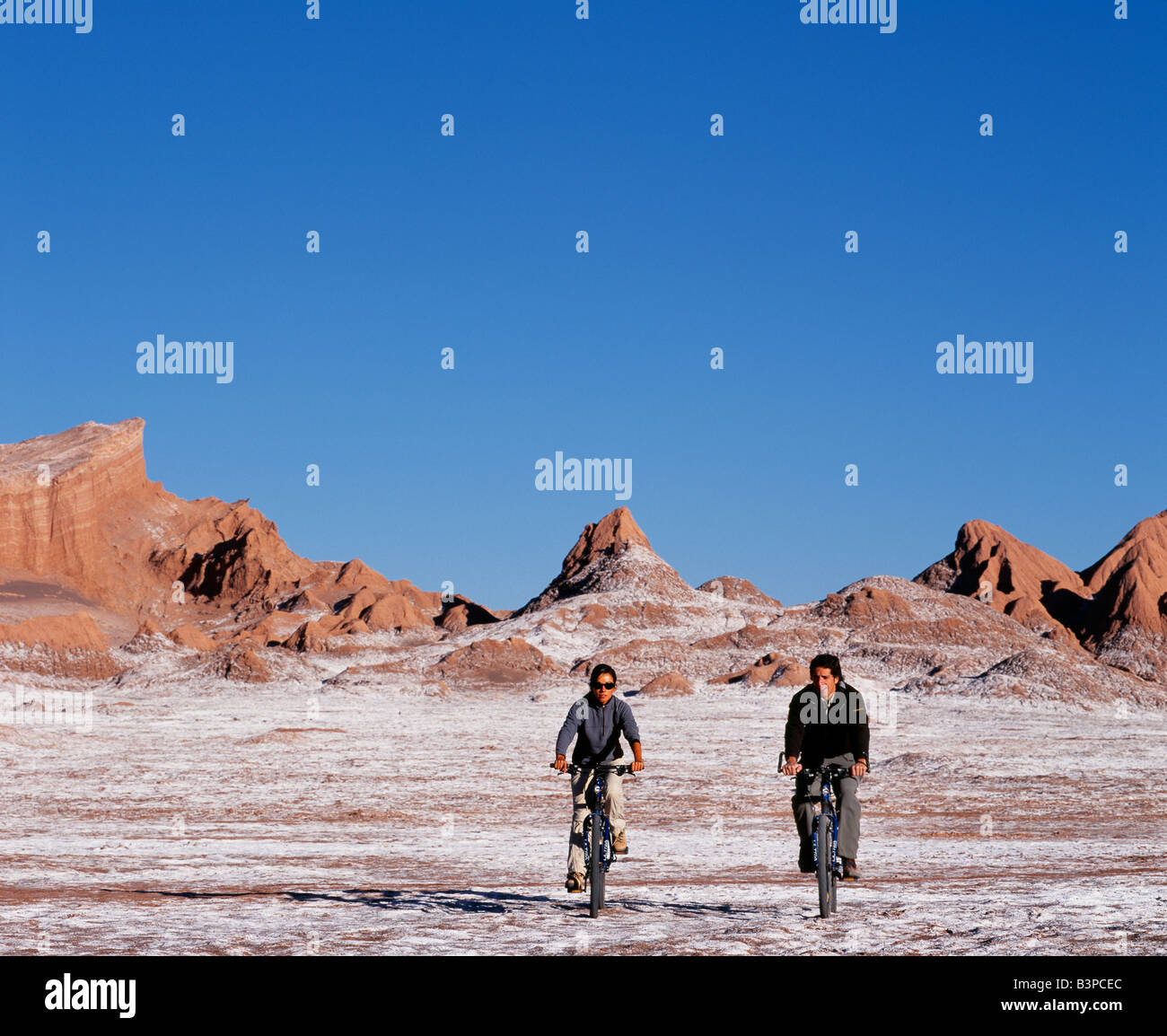 Chile, Atacama-Wüste, San Pedro de Atacama. Touristen-Mountainbiken in der eindrucksvollen Landschaft der Moon Valley in der Nähe von San Pedro de Atacama in der Atacama-Wüste, die geprägt ist von Wind erodiert Hügeln und einem mineralischen Käserand Talboden. Stockfoto