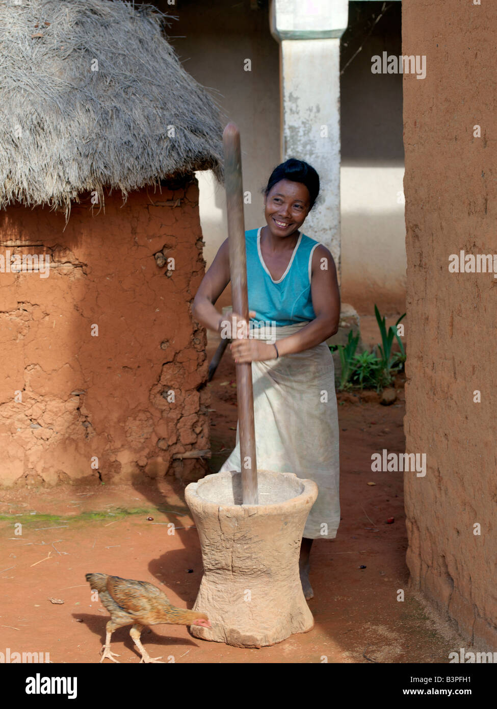 Madagaskar, Southern Highlands, Andohatangona. Eine madagassische Frau schleift einen attraktiven Ma eine hölzerne Stößel und Mörser mit Mais Stockfoto