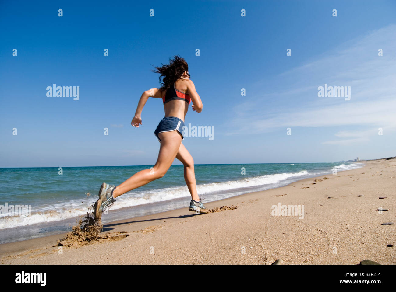 Model Released passen junge Frau, die entlang der Küstenlinie von einer leeren Sandstrand Stockfoto