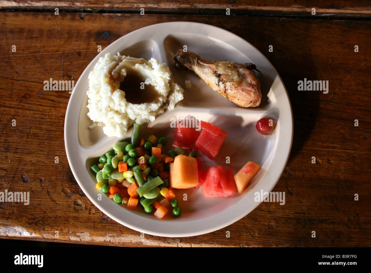 Essen in der Cafeteria, Teller mit Essen, ausgewogen essen, Obstsalat, Hähnchenschenkel, Kartoffelpüree, Gemüse Stockfoto