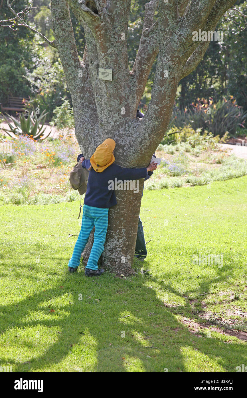 Ein junges Mädchen und ihre Mutter umarmt einen Baum in Kirstenbosch Gardens, Cape Town, Südafrika Stockfoto