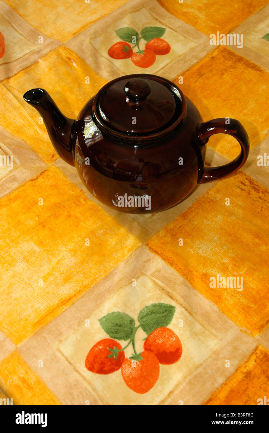 Eine Teekanne sitzt auf einer gelben Kunststoff Tischdecke gemustert mit Erdbeeren. Stockfoto