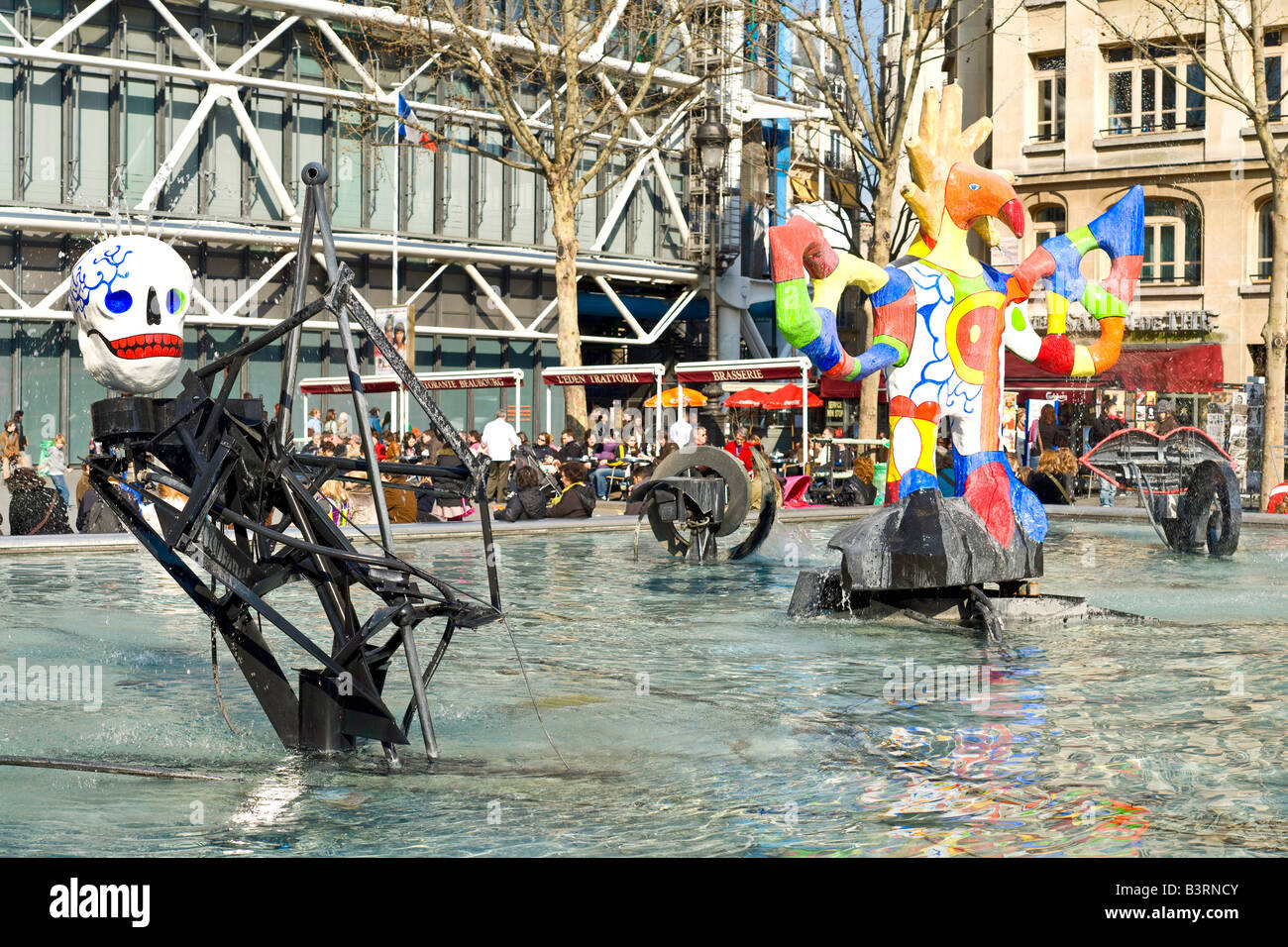 Strawinsky Brunnen Skulpturen Centre Pompidou Paris France // PARIS, Frankreich — der Strawinsky Brunnen (Fontaine Strawinsky) befindet sich neben dem Centre Pompidou auf dem Place Igor Strawinsky im 4. Arrondissement von Paris. Der Brunnen wurde 1983 von den Bildhauern Niki de Saint Phalle und Jean Tinguely geschaffen und zeigt farbenfrohe mechanische Skulpturen, die Themen aus den Werken des Komponisten Igor Strawinsky darstellen. Die verspielte Installation umfasst 16 skurrile, bewegte Skulpturen, die zwischen Wasserstrahlen arbeiten und einen auffälligen Kontrast zur modernen Architektur des Pompidou-Zentrums dahinter bilden. Stockfoto