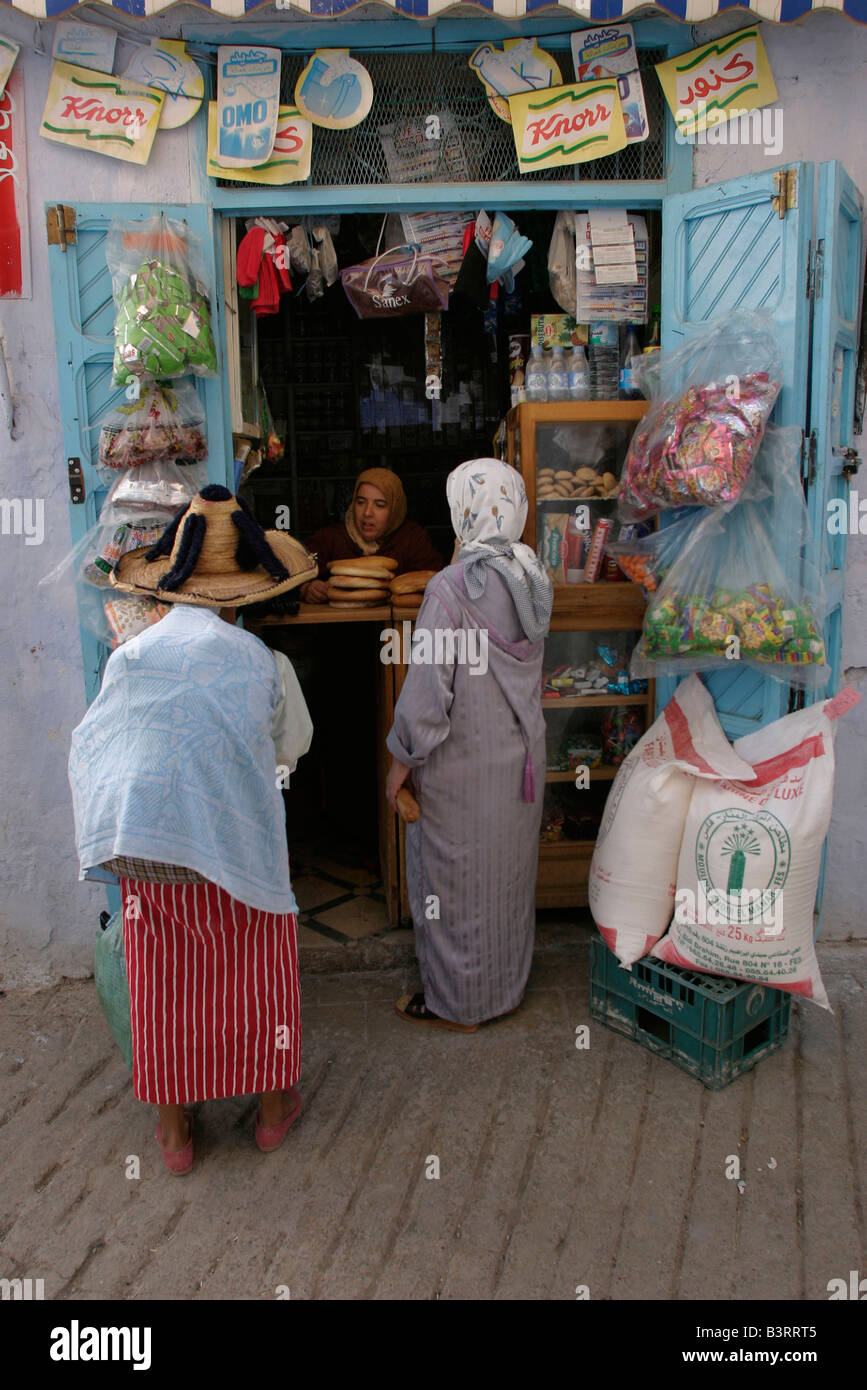 Frauen kaufen Brot und Zubehör aus einem der vielen kleinen Läden in der Fußgängerzonen Gassen des alten Chefchaouen. Stockfoto