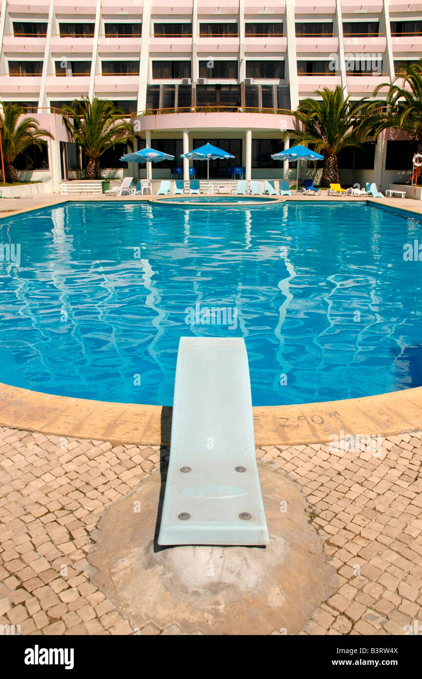 Ein Sprungbrett in einem Hotel-Schwimmbad mit Sonnenschirmen und Hotel Front im Hintergrund. Stockfoto