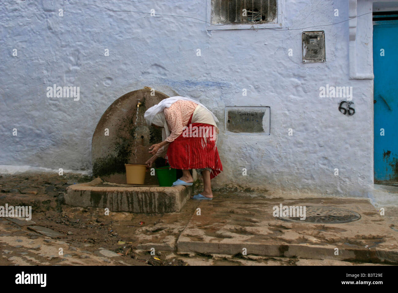 Frau füllt Wasser-Container aus Wasserhahn in der Straße von Chefchaouen.Many Häuser in der Altstadt sind noch ohne fließendes Wasser Stockfoto