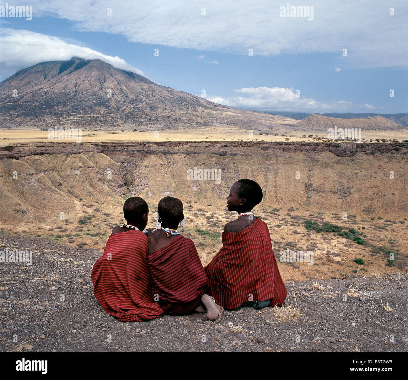 Tansania, Norden von Tansania, drei Maasai Mädchen sitzen am Rande des Shimu la Mungu (ein vulkanischer Schlag Loch bekannt als "Gottes Loch") mit den erloschenen Vulkan, Kerimasi, in der Ferne. Stockfoto