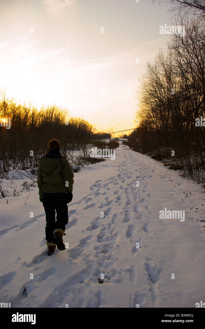Eine Frau geht durch Schnee auf einem Wanderweg in Richtung Sonnenuntergang. Stockfoto
