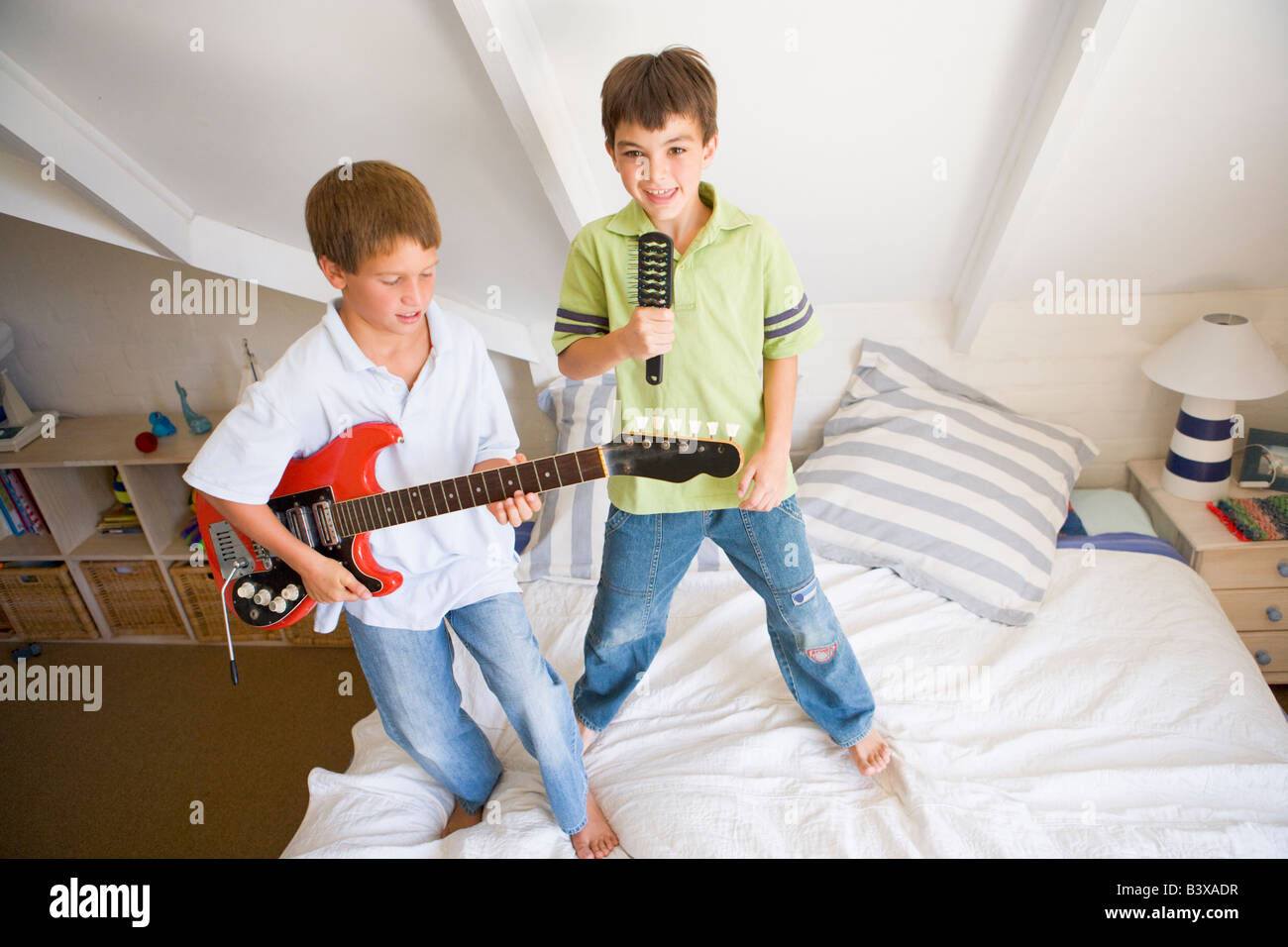 Zwei jungen stehen auf einem Bett, spielt Gitarre und singt in einer Haarbürste Stockfoto
