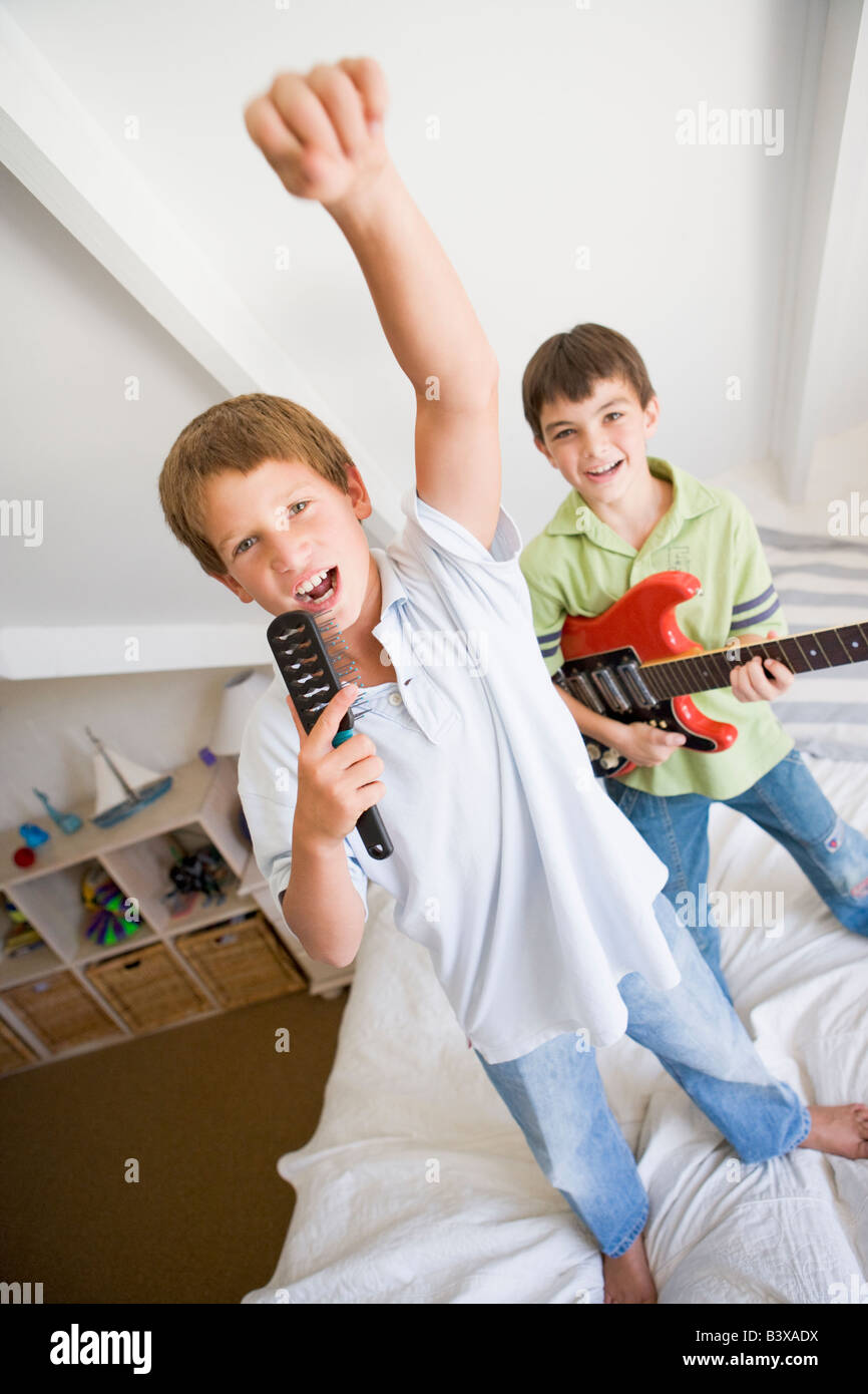 Zwei jungen stehen auf einem Bett, spielt Gitarre und singt in einer Haarbürste Stockfoto