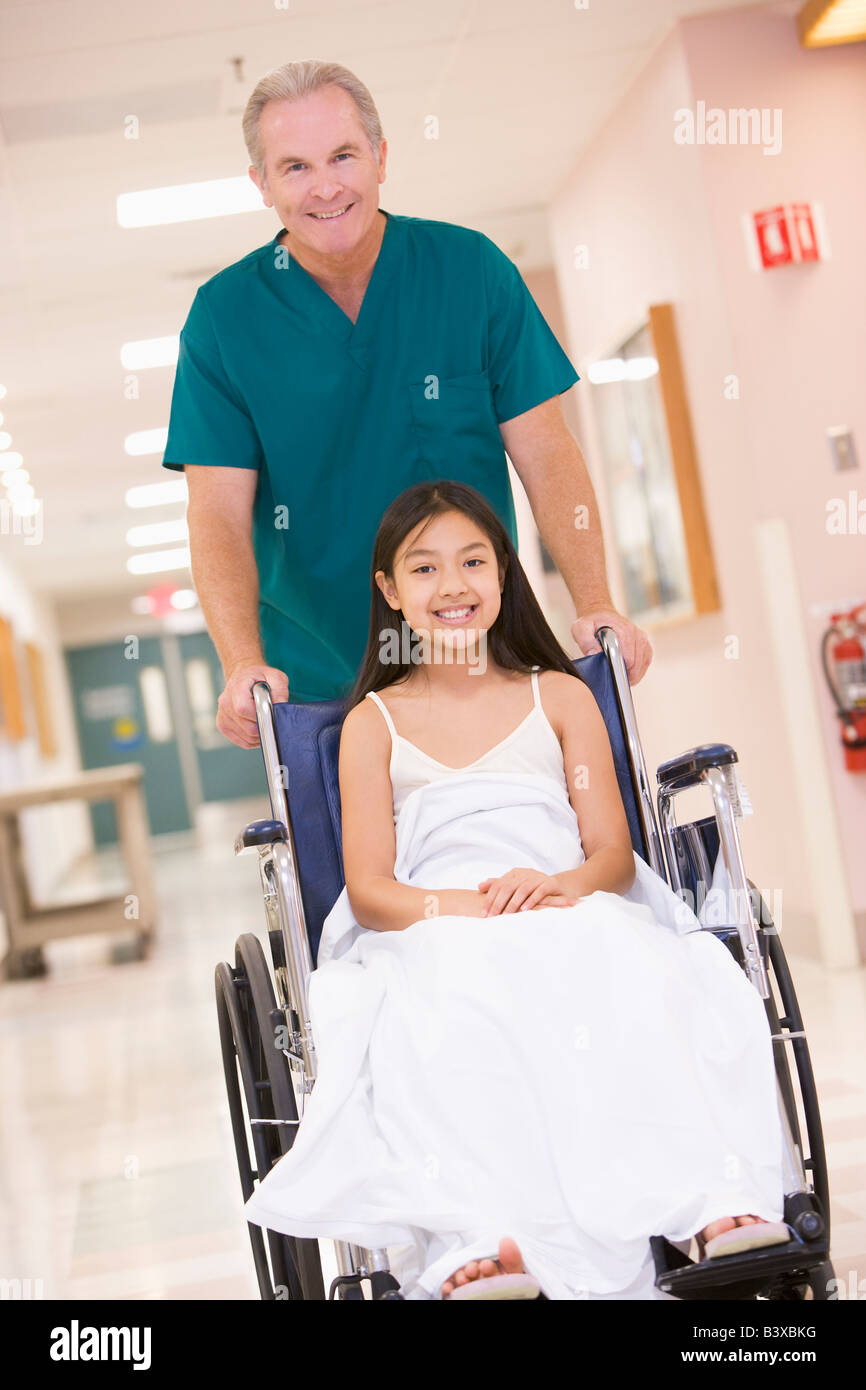 Eine geordnete schieben ein kleines Mädchen im Rollstuhl einen Krankenhaus-Korridor Stockfoto