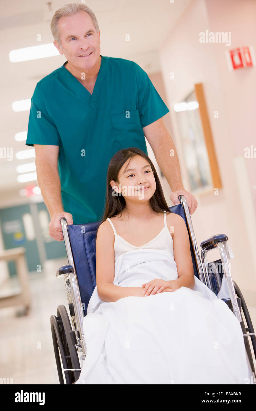 Eine geordnete schieben ein kleines Mädchen im Rollstuhl einen Krankenhaus-Korridor Stockfoto