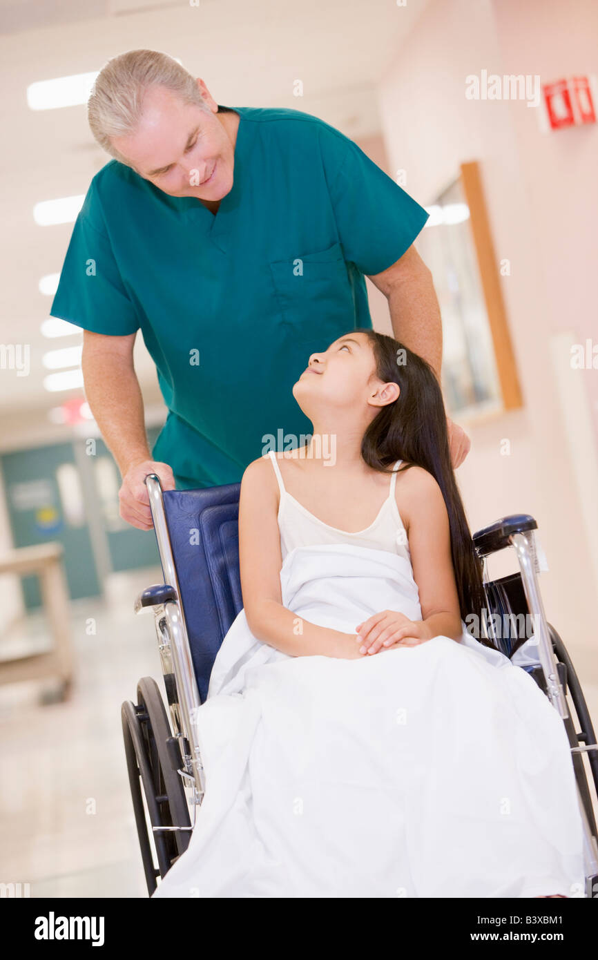 Eine geordnete schieben ein kleines Mädchen im Rollstuhl einen Krankenhaus-Korridor Stockfoto