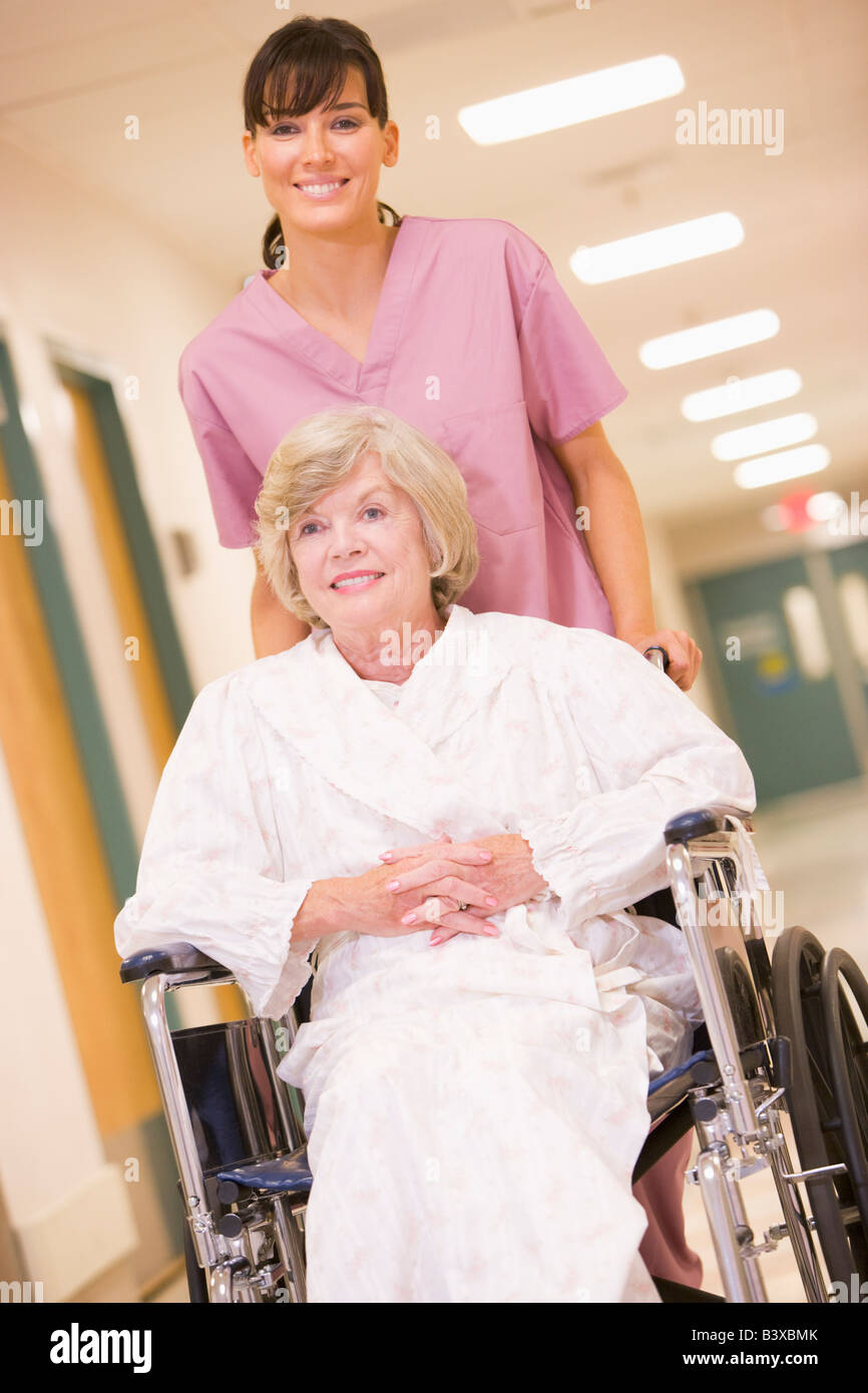Eine Krankenschwester schob eine ältere Frau In einem Rollstuhl einen Krankenhaus-Korridor Stockfoto
