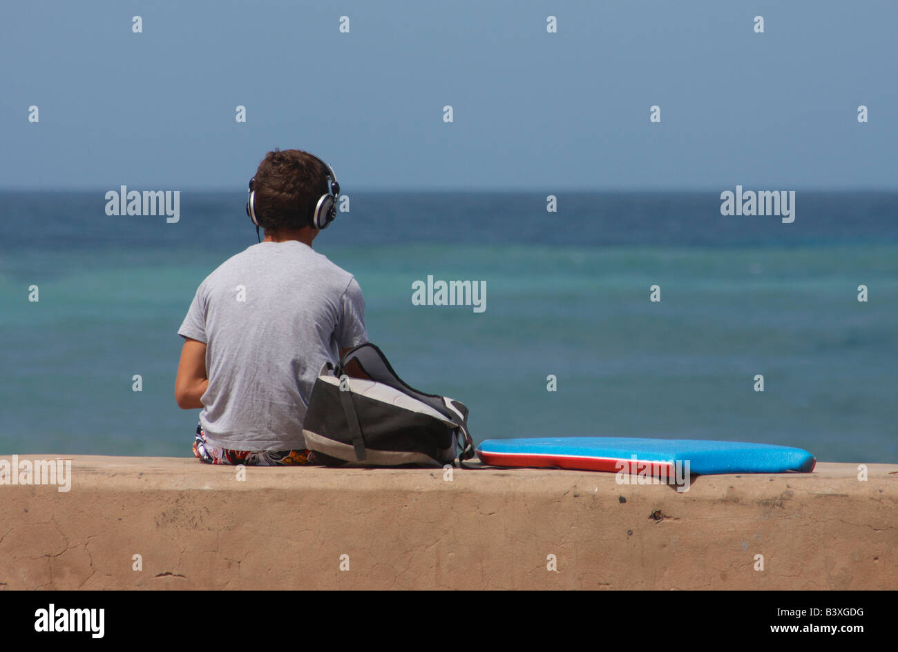 Spanische Teenager Surfer tragen von Kopfhörern und Wellen bei La Cicer, Playa de Las Canteras, Las Palmas, Gran Canaria warten. Stockfoto