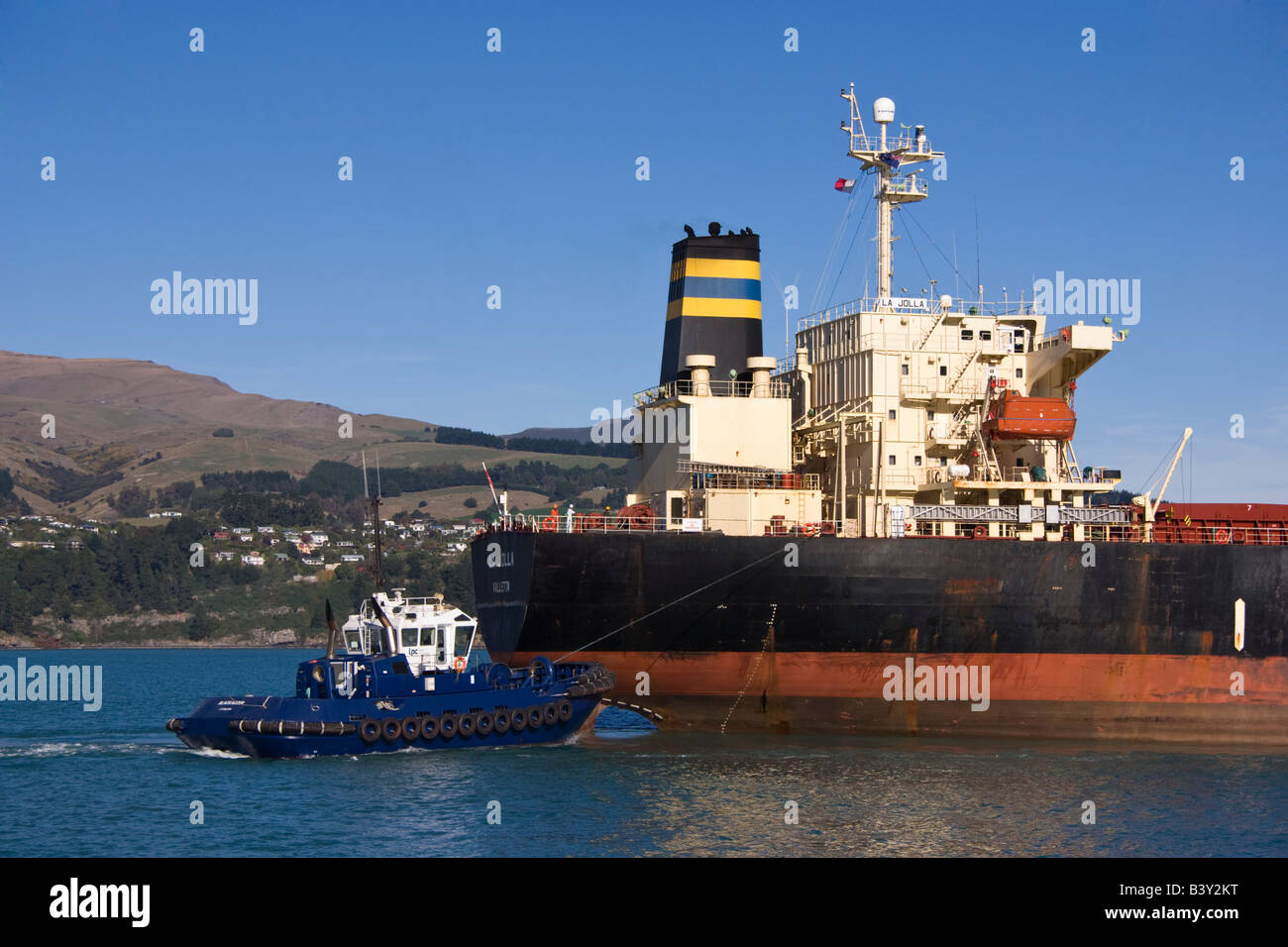 Ein Schlepper hilft am Heck eines Frachtschiffes, wie es im Hafen ankommt. Stockfoto