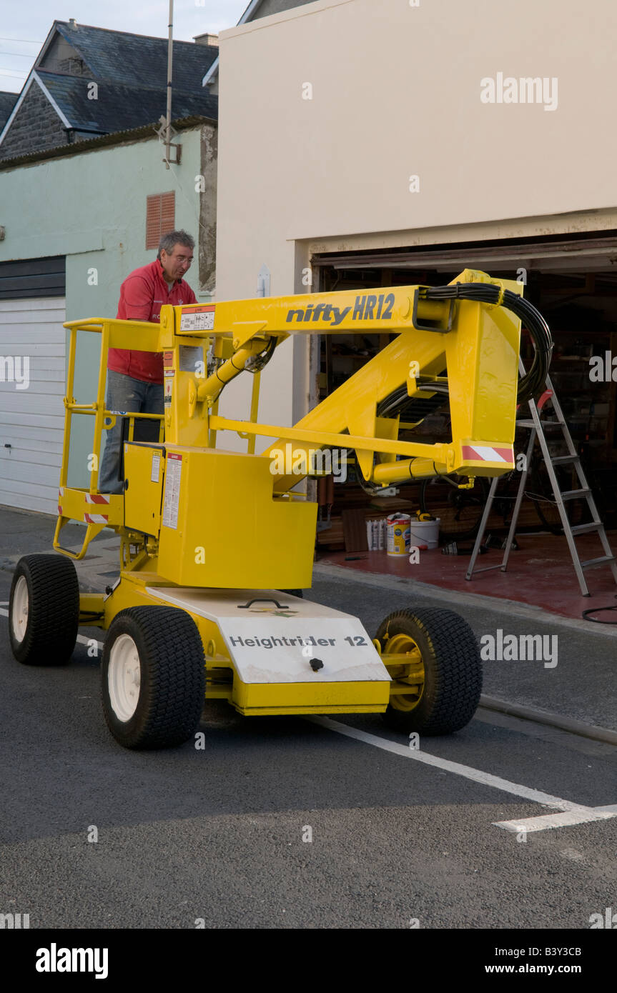 Mann Betrieb eine kleine gelbe motorisierten Selbstfahrer Hubarbeitsbühne erhöhte Plattform für DIY auf seinem Haus oder Wohnung Stockfoto