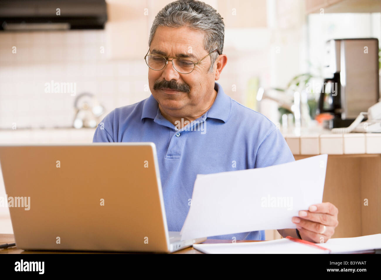 Mann in der Küche mit Laptop und Unterlagen Stockfoto