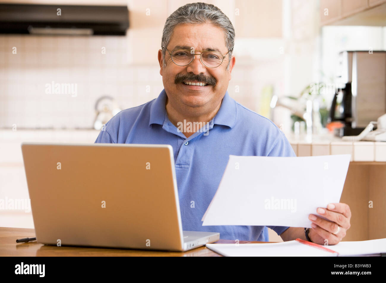 Mann in der Küche mit Laptop und Papierkram lächelnd Stockfoto