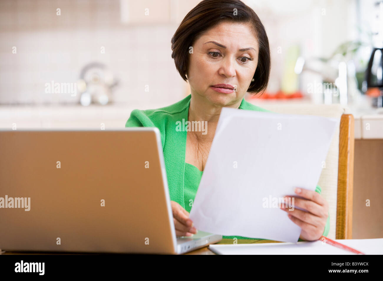 Frau in der Küche mit Laptop und Papierkram schaut besorgt Stockfoto