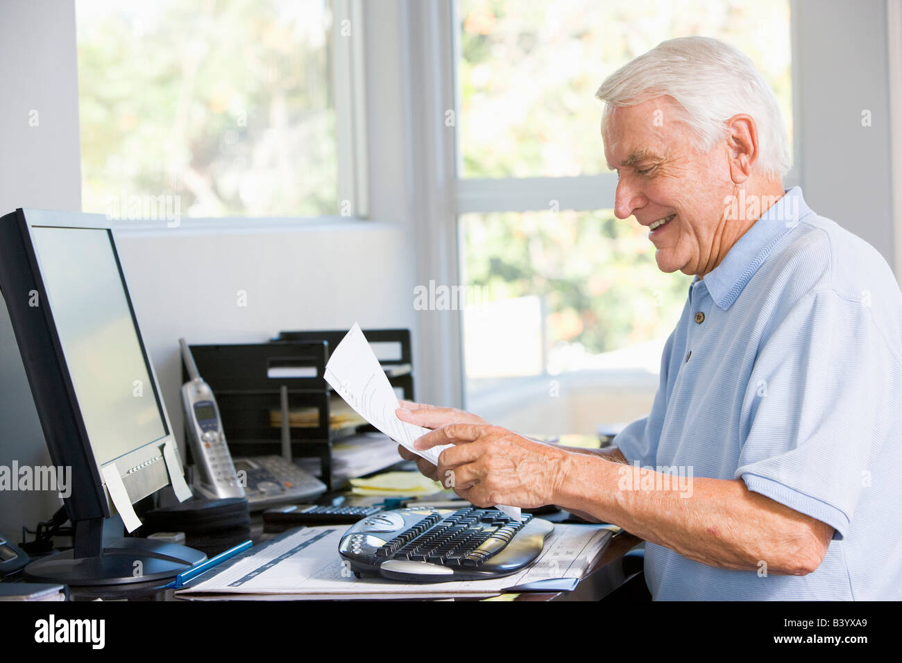 Mann im Büro mit Computer und Papierkram lächelnd Stockfoto