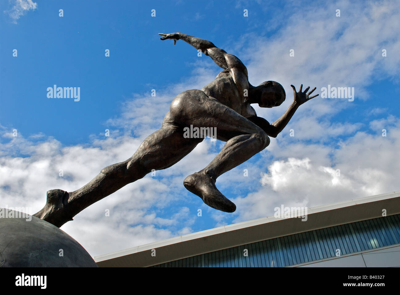 Bronzestatue eines Athleten auf einem Globus von Bildhauer Colin Spofforth, außerhalb SportsCity, Eastlands, City of Manchester Stadium Stockfoto