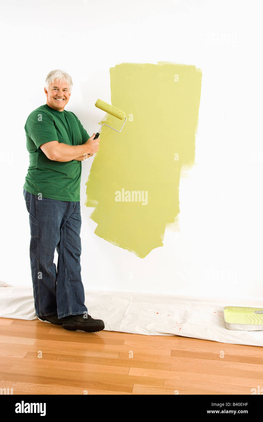 Applying Mann Malerei Wand grün mit Farbroller lächelte viewer Stockfoto