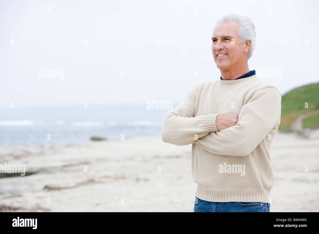 Mann am Strand mit verschränkten Armen lächelnd Stockfoto