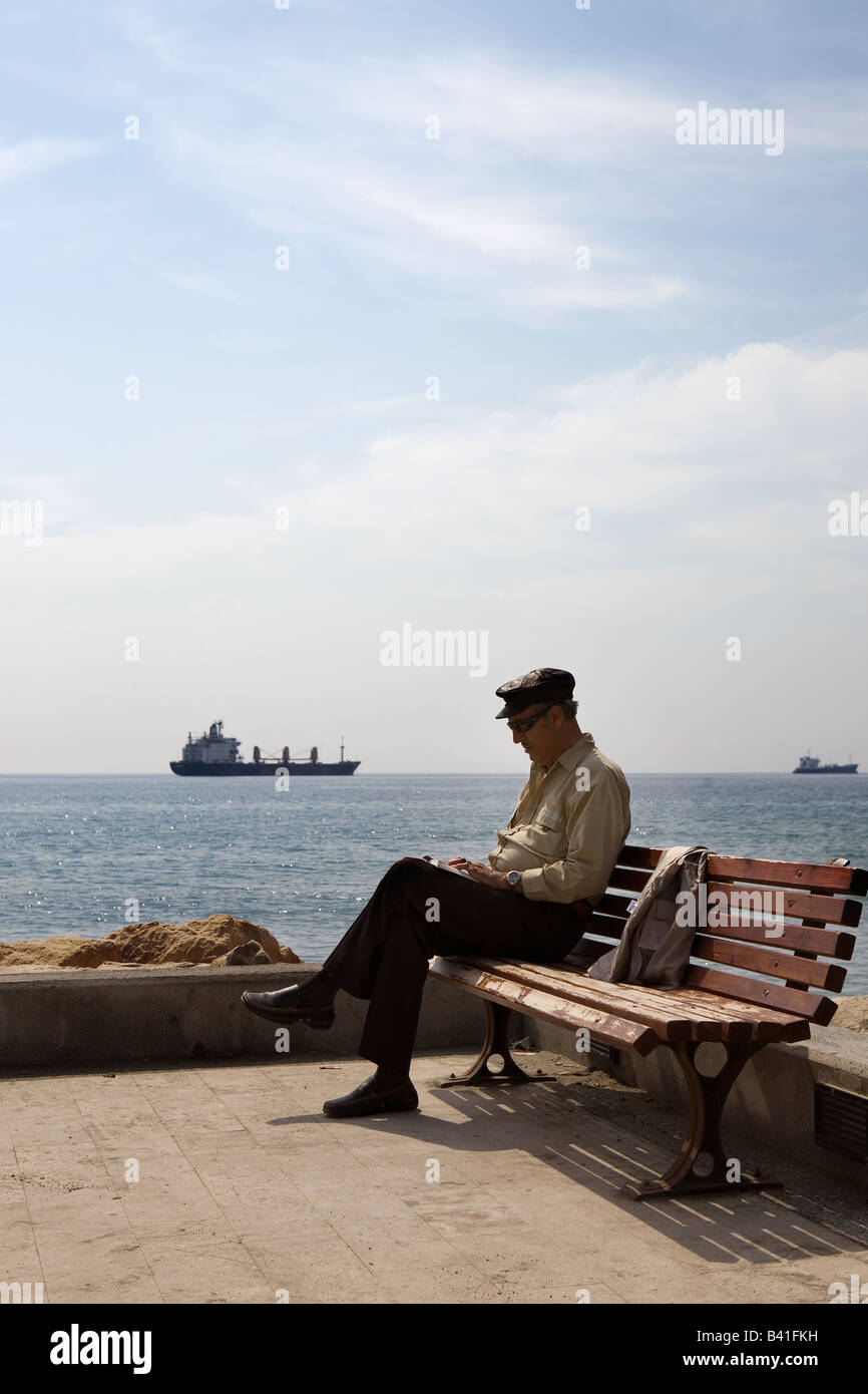 Ein Herr sitzt und liest entlang Limassols Waterfront Promenade auf der Insel Zypern. Stockfoto