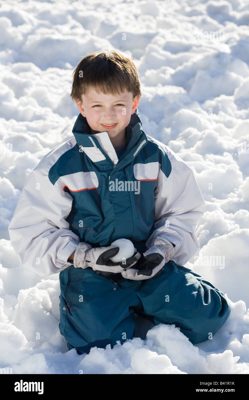Porträt eines knienden jungen hält einen Schneeball. Er trägt einen weißen  und blauen Skianzug und weiße Handschuhe, draußen im Schnee Stockfotografie  - Alamy