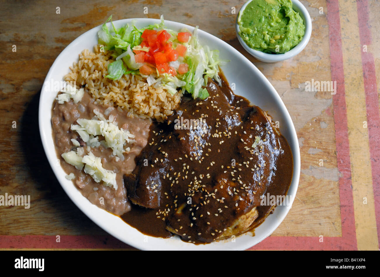 Chicken Enchiladas mit einer Mole Poblano Sauce und Reis und Bohnen mit Käse und eine Beilage der Guacamole. Stockfoto