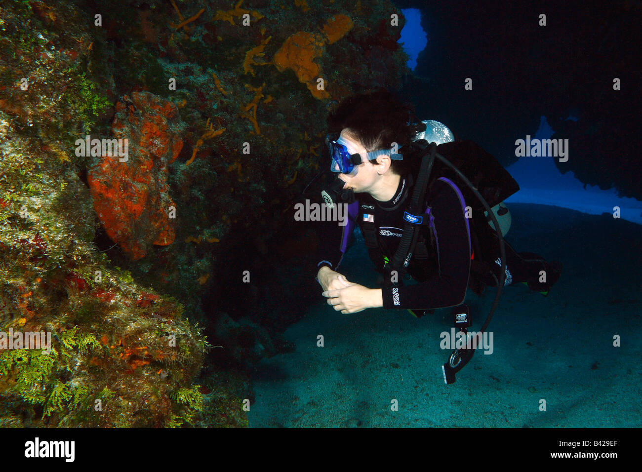 Eine einzelne weibliche Taucher massive Korallenriff Formationen mit Höhlen und schwimmen durch Tunnel zu erkunden. Stockfoto