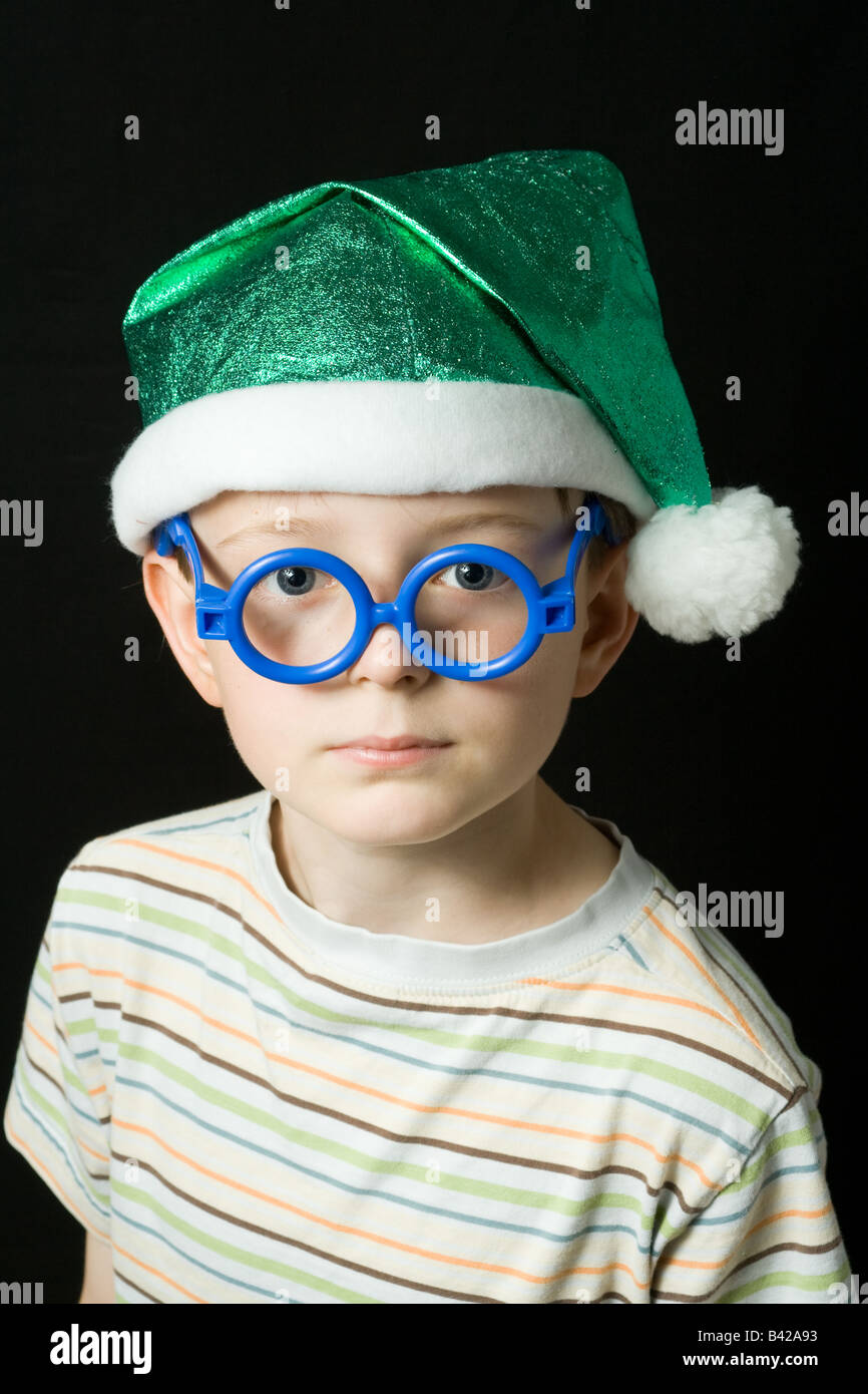 Ein kleiner Junge mit grünen Weihnachtsmütze Elf blaue Gläser und weiße Quaste; Porträt vor einem schwarzen Hintergrund isoliert. Stockfoto