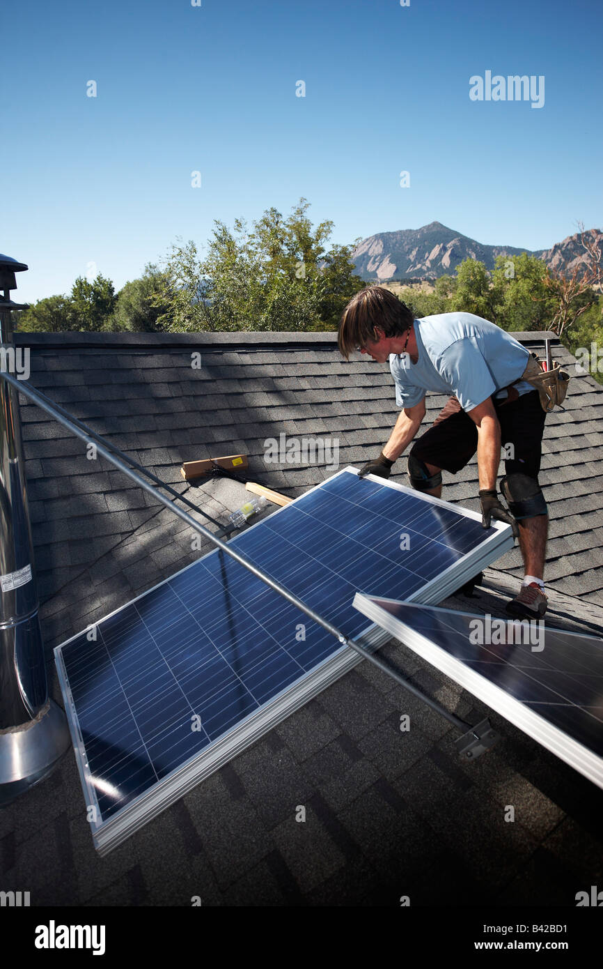 Ein Mann, ein Array von Sonnenkollektoren auf dem Dach seines Hauses installieren. Stockfoto