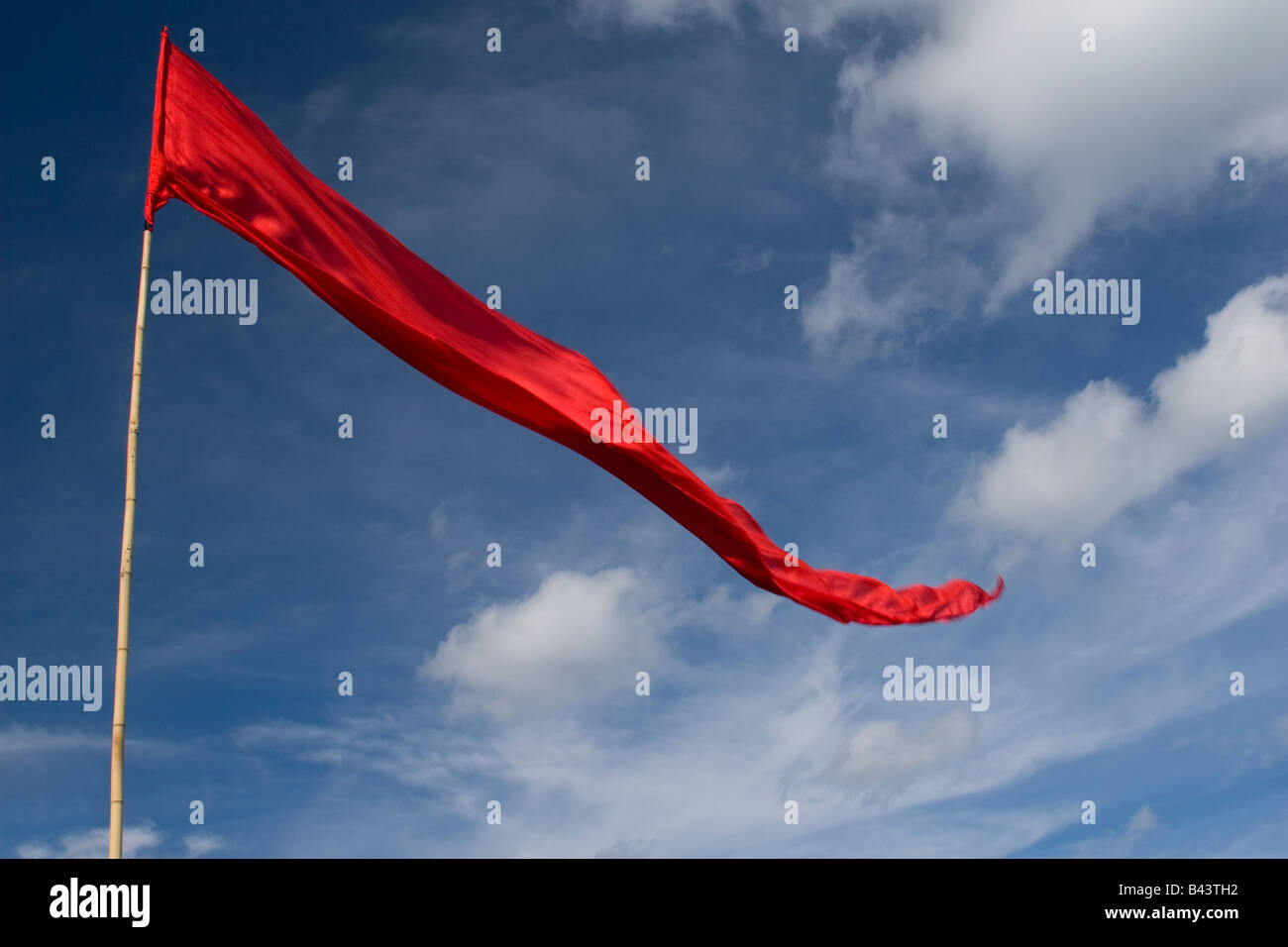 Eine sehr lange rote Fahne vor blauem Himmel mit weißen Wolken geschwollen. Stockfoto