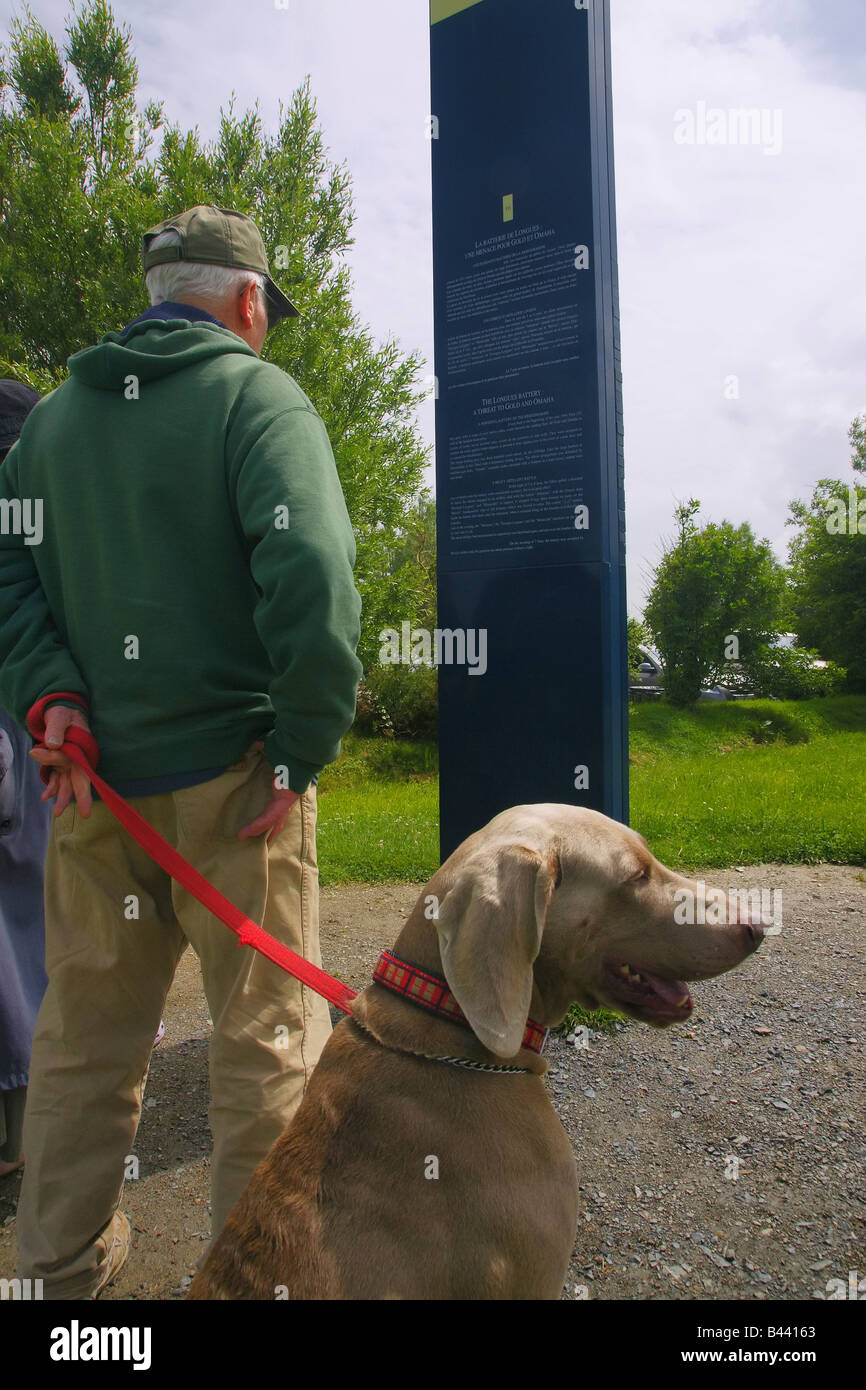 Normandie, Frankreich. Ein Mand und seinen Hund beobachten ein Denkmal Zeichen in La Madeleine Marinegeschütz Batterie. Stockfoto