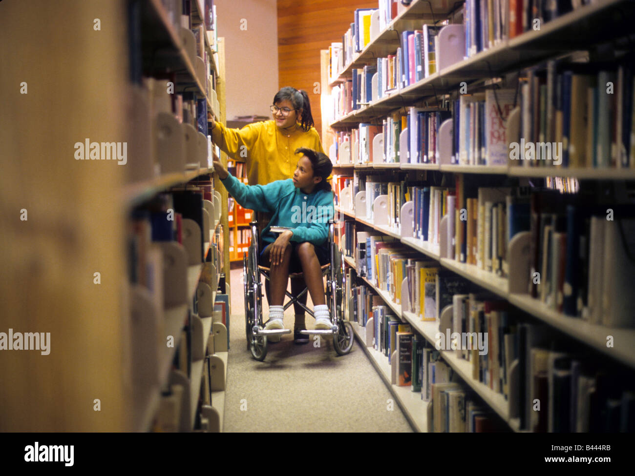 Junges Teenies Mädchen hilft Freund im Rollstuhl ausgewählte Buch in Bibliothek. Stockfoto
